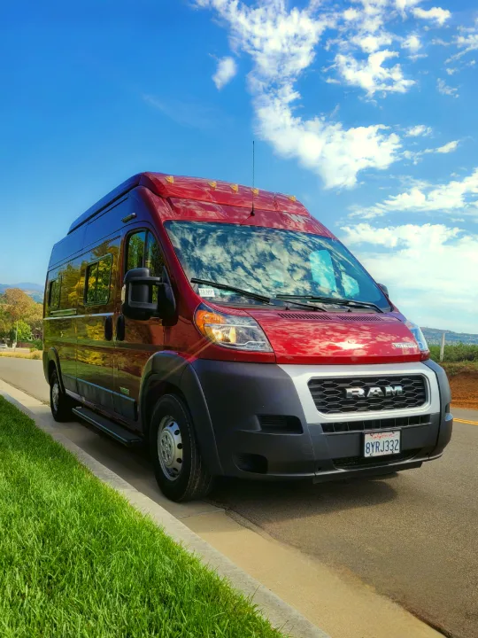 Stylish red Ram ProMaster RV rental parked curbside on a sunny day. Ready for adventure!. Winnebago Solis 2022
