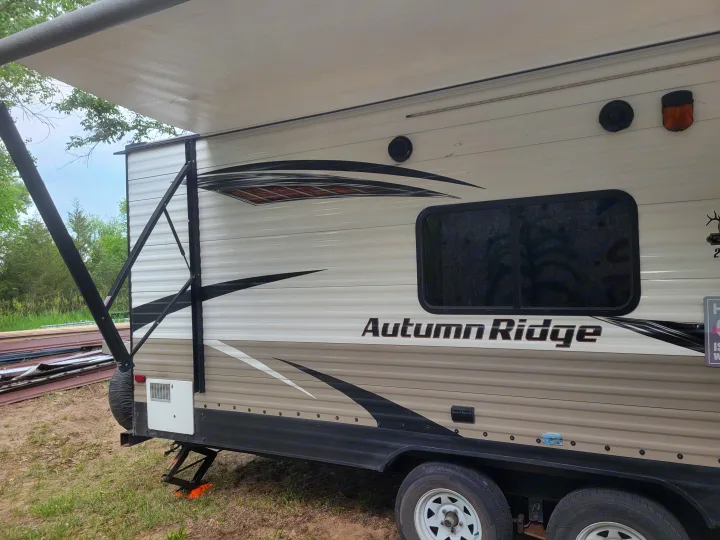 This Autumn Ridge travel trailer RV rental, with its awning extended, is set up in a natural outdoor campsite.. Starcraft Autumn Ridge 2018