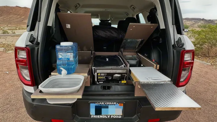 Rear view of an SUV with a custom camper setup, ideal for an RV rental adventure. Organized storage, water, and pull-out table are visible.. Ford Bronco Sport 2022