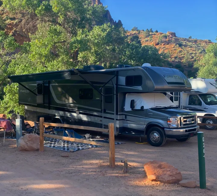 Relaxing at a picturesque campsite with an RV rental, featuring an extended awning, nestled among vibrant green trees and red rock cliffs.. Forester Classic 2021