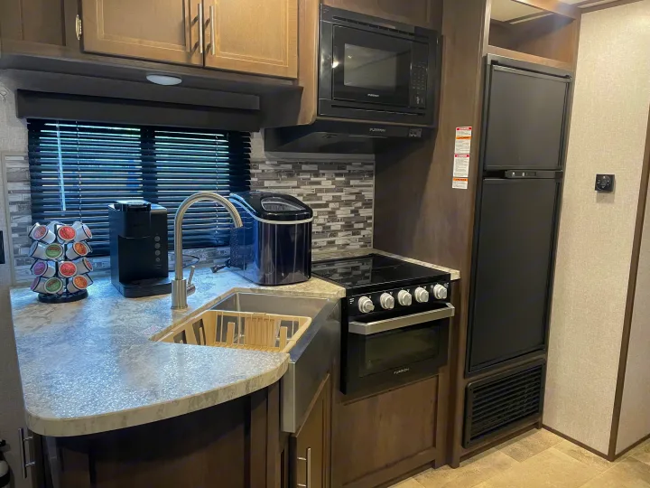 RV rental kitchen with modern appliances: sink, Keurig, ice maker, Furrion microwave, oven, and full-size refrigerator.. Dutchmen Coleman Lantern 2019