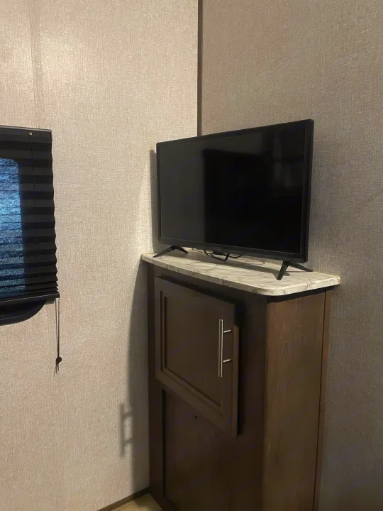 RV rental interior: A Vizio TV on a cabinet with storage and a marble-look counter. Includes a window with a blind.. Dutchmen Coleman Lantern 2019