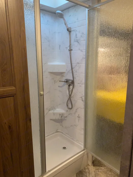 This RV rental offers a modern shower with white marbled walls, a handheld showerhead, and frosted glass doors, ideal for travel.. Forester Classic 2021