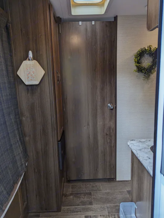 Interior of an RV rental showing dark wood-grain walls, a closed door, skylight, and a "Collect Adventures" sign. Cozy, compact travel space.. Keystone RV Bullet Crossfire 2018