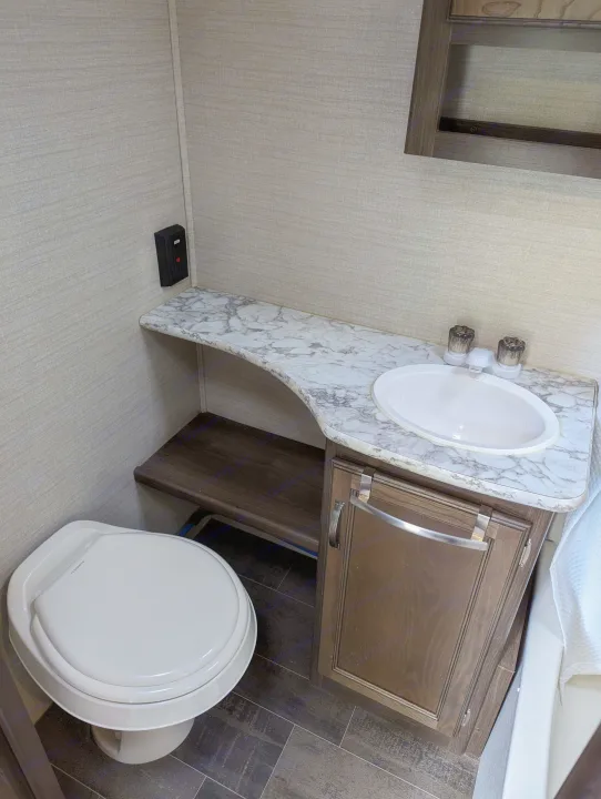 Compact RV rental bathroom with white toilet, sink, and marbled counter, plus dark wood cabinet and floor.. Keystone RV Bullet Crossfire 2018