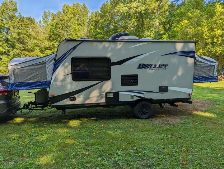 Bullet Crossfire hybrid travel trailer RV rental set up for camping, featuring pop-out tent beds and its tow vehicle.. Keystone RV Bullet Crossfire 2018