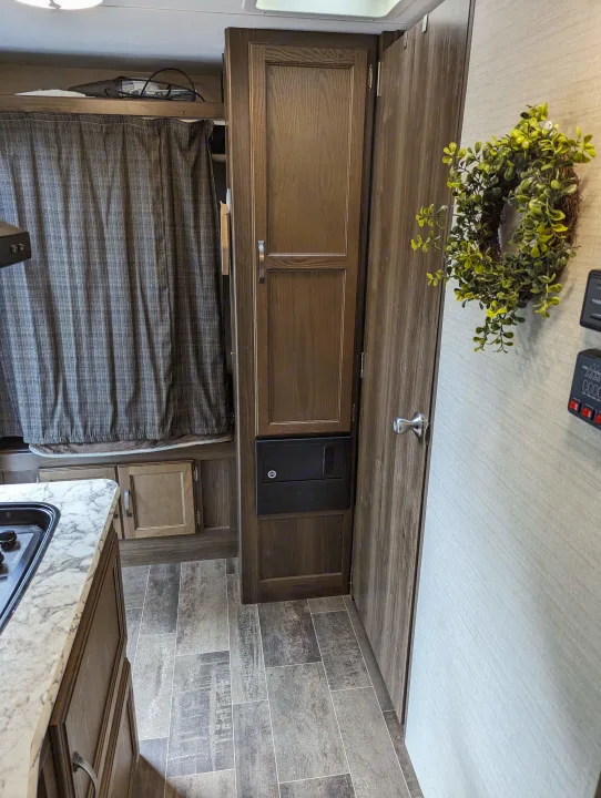 RV rental interior: Kitchen counter, central storage, electrical panel, and control panel by a door with a wreath. Cozy camper.. Keystone RV Bullet Crossfire 2018