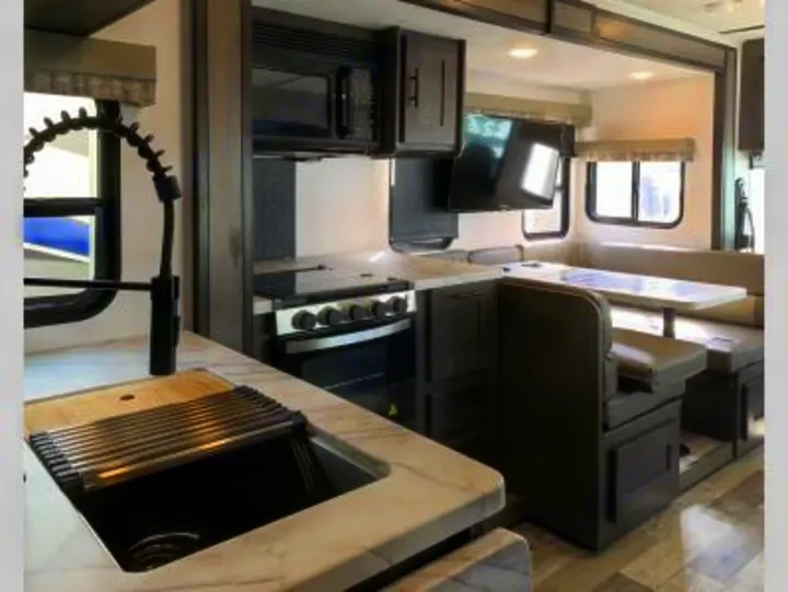 Modern RV rental interior featuring a full kitchen with sink, stove, microwave, and a comfortable U-shaped dinette.. FR3 32DS 2024