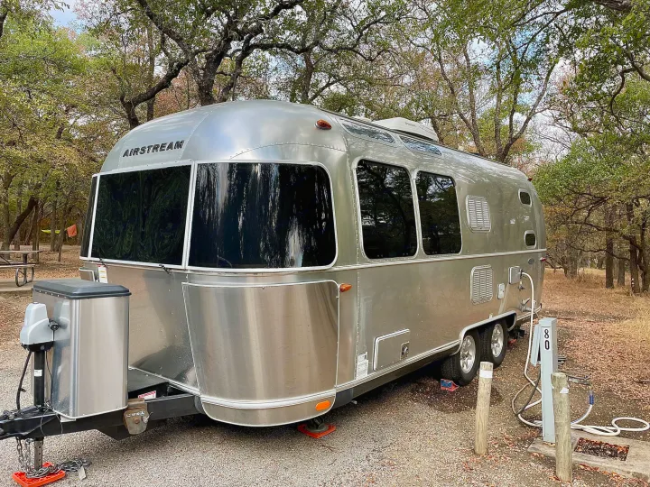 A shiny Airstream travel trailer, great for an RV rental, set up at a quiet, tree-filled campsite with hookups.. Airstream Flying Cloud 2016