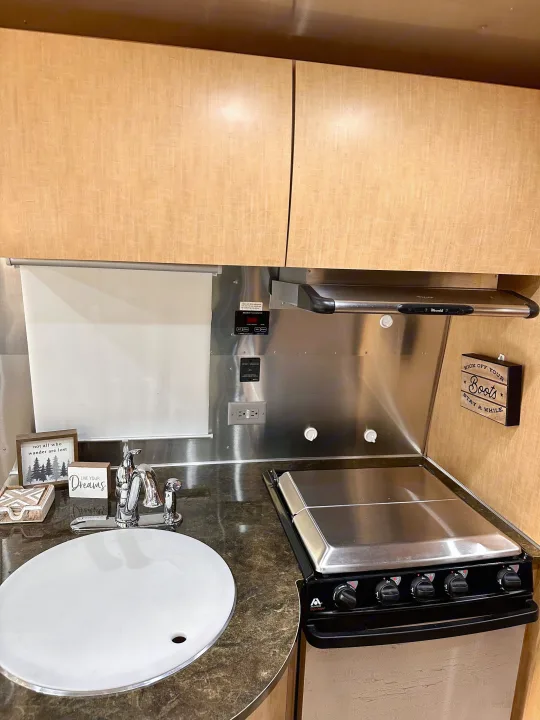 A functional RV rental kitchen with a small sink, stove, light wood cabinets, and stainless steel backsplash.. Airstream Flying Cloud 2016