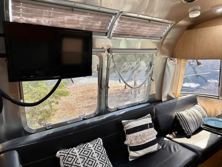 Comfortable Airstream rv rental interior: modern black seating, large windows with scenic views, and a wall-mounted TV.. Airstream Flying Cloud 2016
