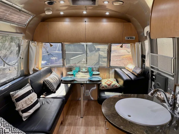 Cozy Airstream rv rental interior: dining area with set table and banquette seating, plus a foreground kitchenette.. Airstream Flying Cloud 2016