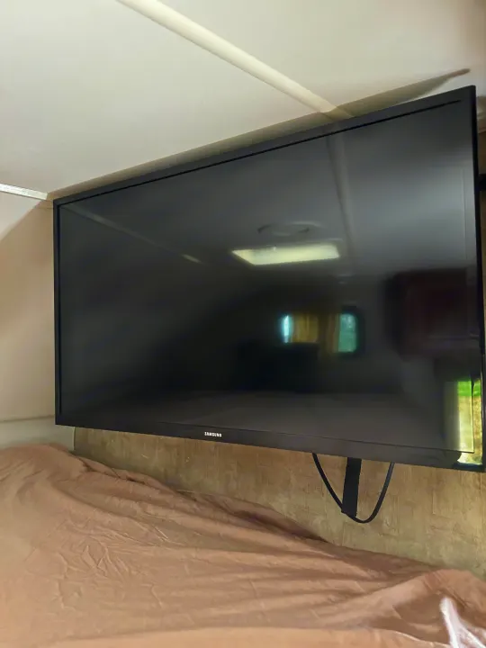 RV rental interior: Mounted Samsung TV above bed, reflecting ceiling light, window, and cabinet.. Winnebago Minnie Winnie 2014