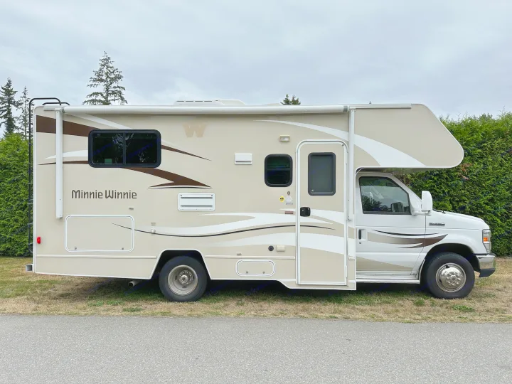 Beige Minnie Winnie RV rental: a spacious motorhome with brown accents, parked on grass under a cloudy sky.. Winnebago Minnie Winnie 2014
