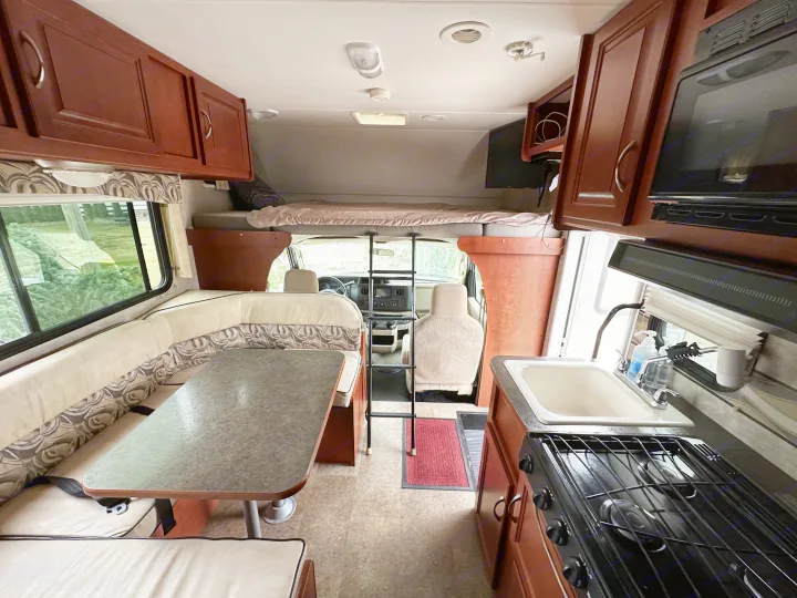 The RV rental interior features a kitchen with sink and stove, dinette, and cab-over bed. Ready for adventures!. Winnebago Minnie Winnie 2014