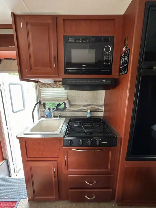 RV rental kitchen: This compact space has a sink, microwave, stovetop, and ample wood cabinets for convenient mobile living.. Winnebago Minnie Winnie 2014