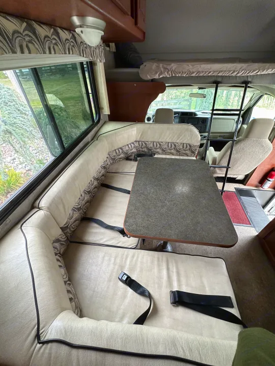 View inside an RV rental showing a comfortable dinette with seatbelts, an over-cab bunk bed, and the driver's area.. Winnebago Minnie Winnie 2014
