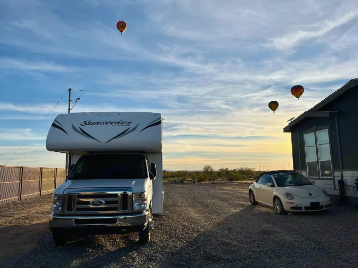 RV rental and convertible parked in a desert setting with three hot air balloons ascending at sunset.. Forest River Sunseeker 2017