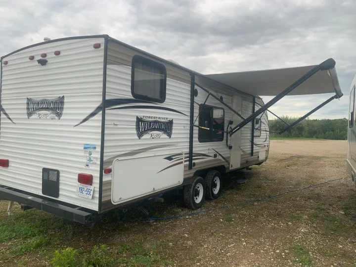 This Forest River Wildwood X-Lite travel trailer, ideal for rv rental adventures, is parked with its awning extended on a gravel lot.. Forest River Wildwood X-Lite 2017