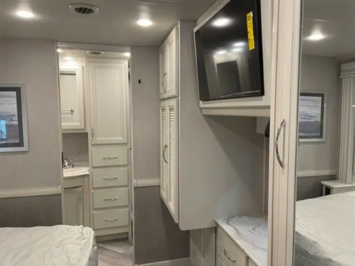Explore this RV rental's bedroom, featuring a mounted TV, integrated vanity with sink, and ample built-in storage.. Fleetwood Other 2022