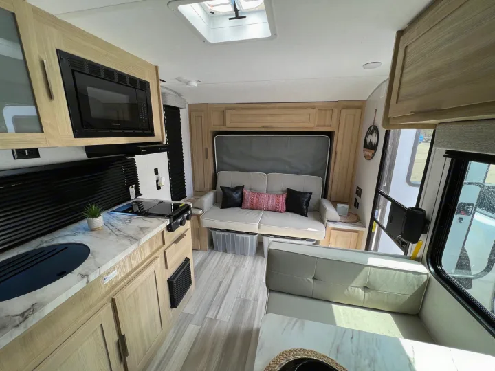 Step inside this modern RV rental! Features a compact kitchen, sofa, dining booth, and sleek light wood cabinetry.. Forest River Salem FSX 2023