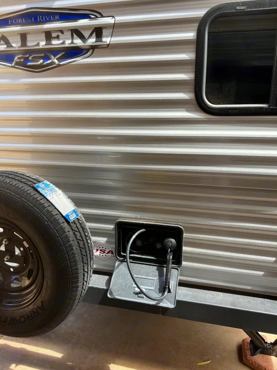 Side of an RV rental showing its Forest River Salem FSX branding, mounted spare tire, and open outdoor shower.. Forest River Salem FSX 2023