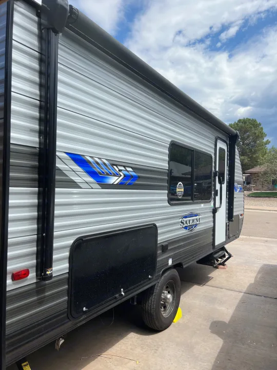 Gray RV rental travel trailer with blue accents, parked on a concrete driveway under a cloudy sky.. Forest River Salem FSX 2023