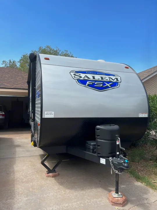 Front view of a shiny gray Forest River Salem FSX travel trailer, a great option for RV rental, parked on a concrete driveway.. Forest River Salem FSX 2023