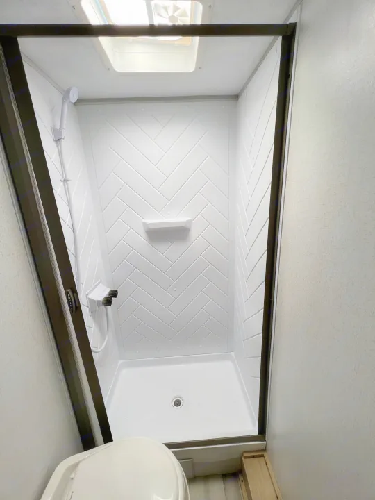 Modern, bright white shower with herringbone walls and a skylight in an RV rental bathroom.. Forest River Salem FSX 2023