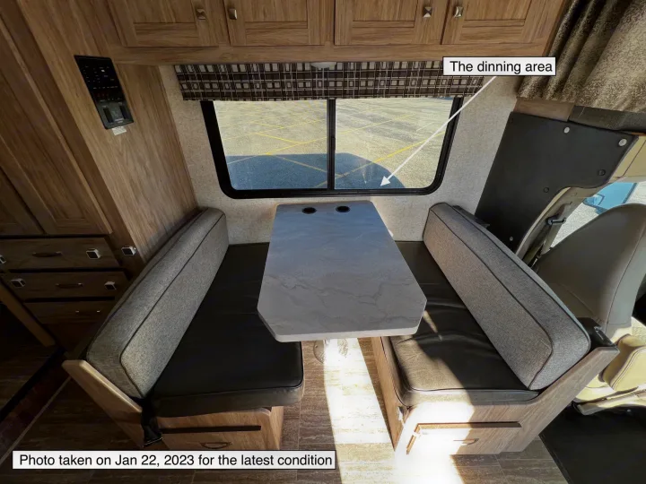 Inside an RV rental, showing the cozy dinette area with a table, benches, and a large window overlooking a parking lot.. Forest River Sunseeker LE 2020