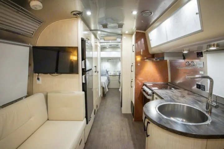 Explore this spacious RV rental interior, showcasing a comfortable lounge, full kitchen, and private bedroom for your travels.. Airstream International 2020