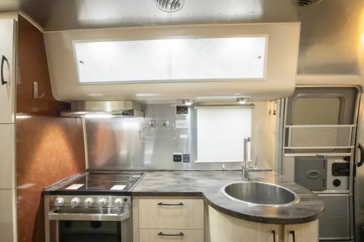Explore this modern RV rental kitchen, featuring a full stove, sink, and ample countertop space for your travels.. Airstream International 2020