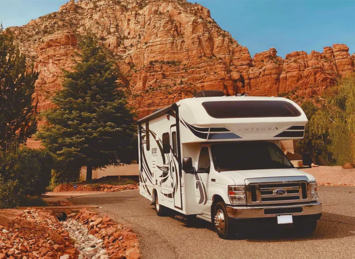 Scenic RV rental adventure! White motorhome parked before impressive red rock formations & green trees under a clear blue sky.. Entegra Coach Odyssey 2020