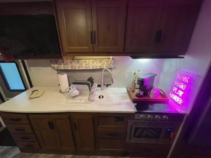 Modern RV rental kitchen featuring a sink, stove, coffee station, and cabinets, well-lit with ambient light.. Forester Classic 2021