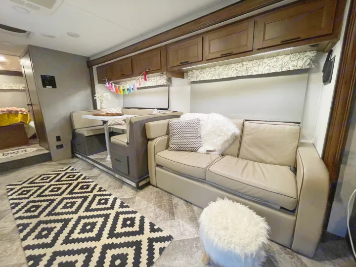 Modern RV rental living space featuring a comfy sofa with pillows, a dining booth, and a geometric rug creating a cozy interior.. Forester Classic 2021