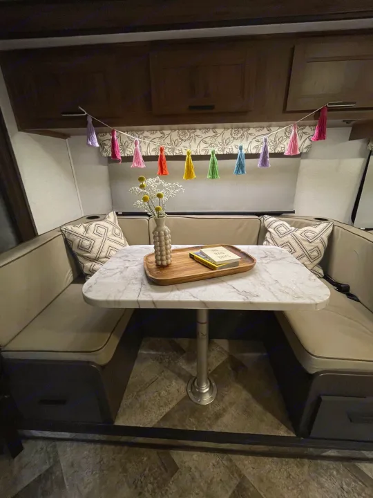 Inside a chic RV rental: a bright dinette with a marble table, flowers, books, and colorful tassels. Ready for your next travel adventure!. Forester Classic 2021