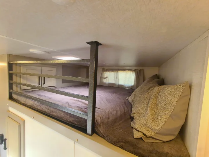 Cozy RV rental bunk bed area with a metal safety rail, soft bedding, overhead lights, and storage cabinets.. Palomino Columbus 2022