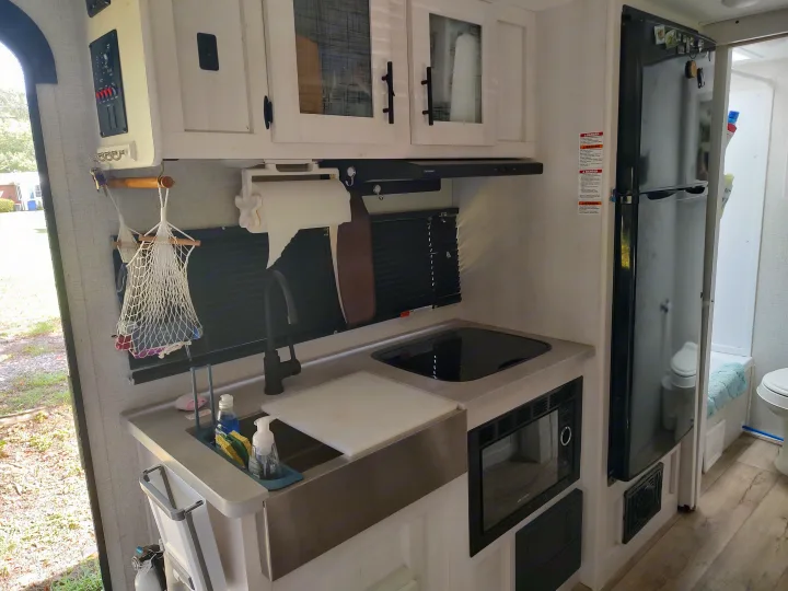 Inside an RV rental: a compact kitchen area featuring a sink, cooktop, microwave, and refrigerator, complete with overhead cabinets.. Dutchmen Coleman Rubicon 2021