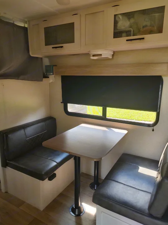 This RV rental features a comfortable dinette area with black benches, a light wood table, and overhead cabinets, perfect for meals on the go.. Dutchmen Coleman Rubicon 2021