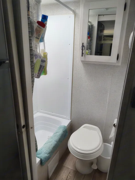 Inside an RV rental, a compact bathroom featuring a shower, toilet, and wall-mounted mirror with toiletries.. Dutchmen Coleman Rubicon 2021