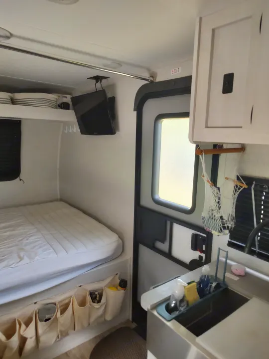Compact RV rental interior featuring a comfortable bed, TV, kitchen sink area, and door, ideal for road trips.. Dutchmen Coleman Rubicon 2021