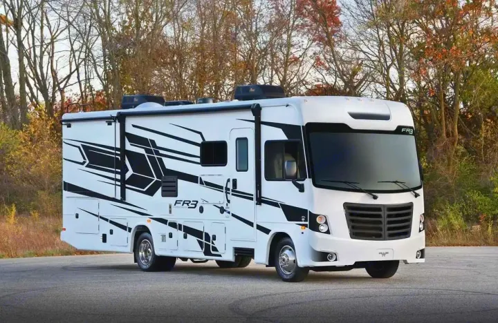 White RV motorhome with black graphics, ready for RV rental adventures. Parked on asphalt amidst trees, this recreation vehicle is for travel.. Forest River 34DS 2022