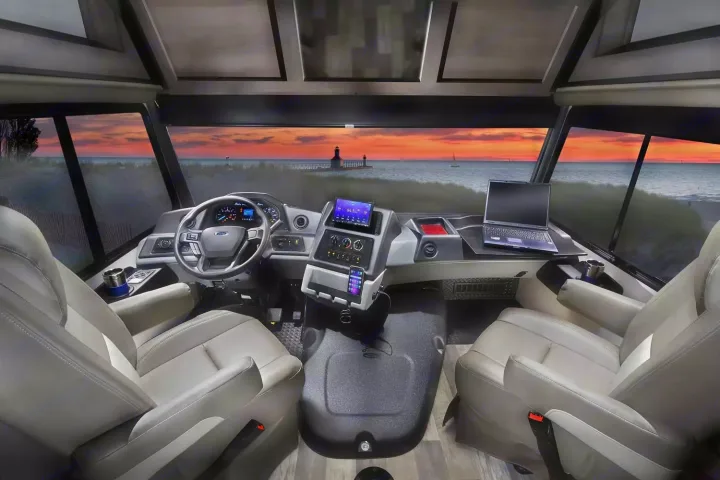 Inside an RV rental: modern cockpit with driver/passenger seats, dashboard, and a laptop, enjoying a beach sunset.. Forest River 34DS 2022