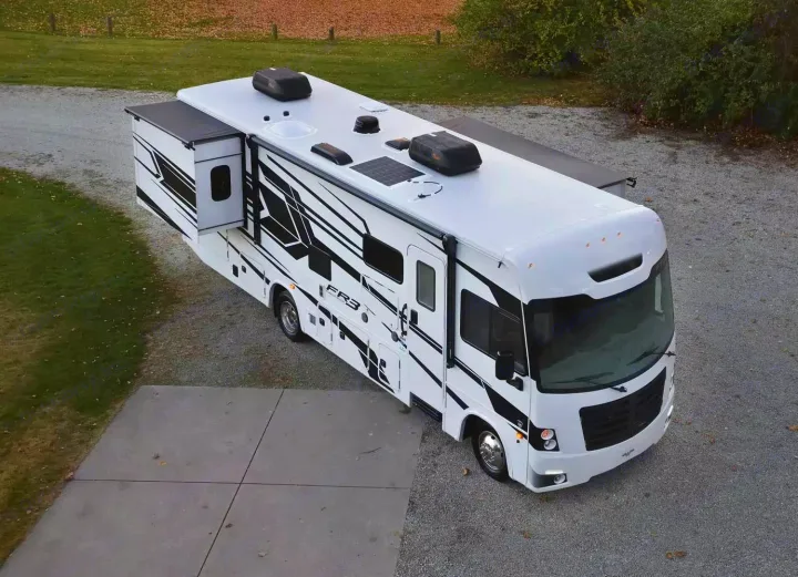 Overhead view of a large white RV rental with black decals, slide-out and awning extended on gravel. Ready for travel.. Forest River 34DS 2022