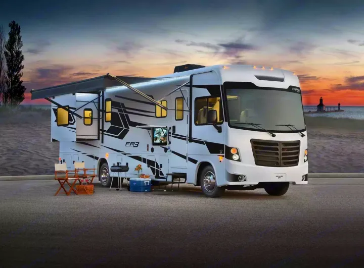Spacious white FR3 RV rental on asphalt by a beach at sunset, with an extended awning and outdoor setup.. Forest River 34DS 2022