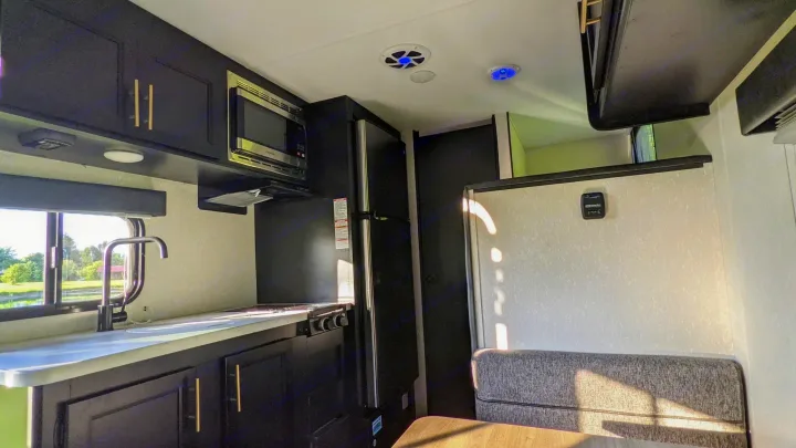Inside this stylish RV rental, a compact kitchen features black cabinets, sink, microwave, and a cozy dining area.. Cherokee wolf pup 2021