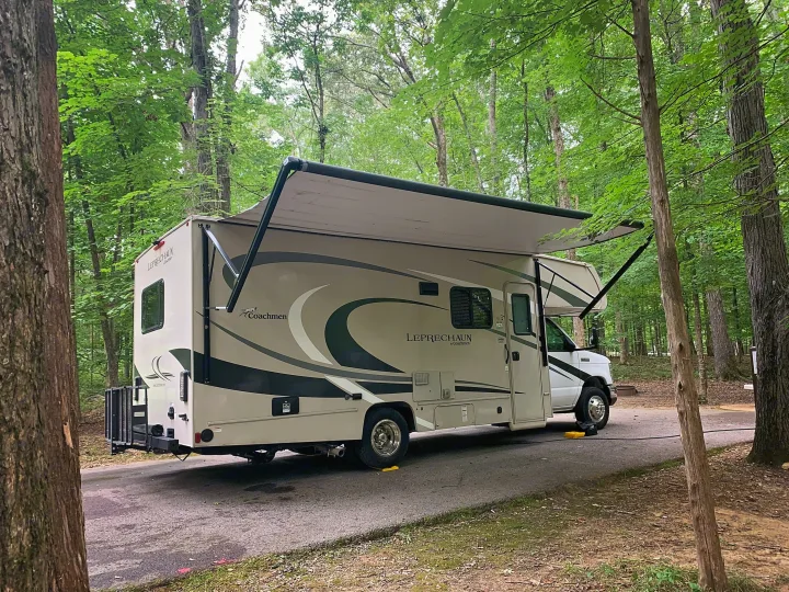 Coachmen Leprechaun RV rental, parked with awning extended at a wooded campsite, surrounded by trees.. Forest River Coachmen Leprechaun 2020