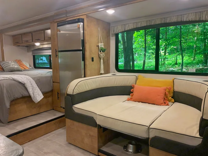 Cozy RV rental interior with a bed, stainless steel fridge, and a dinette overlooking a lush forest.. Forest River Coachmen Leprechaun 2020