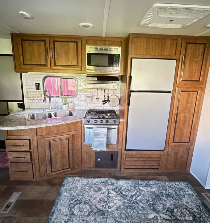 A compact rv rental kitchen featuring warm wood cabinets, double sink, stove, fridge, and subway tile backsplash.. Crossroads RV Zinger 2017