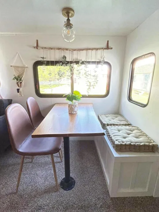 Cozy RV rental dining area: wood table, modern chairs, bench with cushions, and charming plant decor near windows.. Crossroads RV Zinger 2017